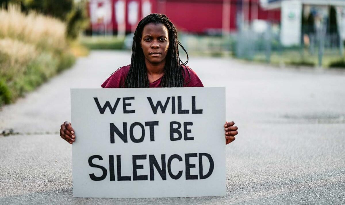 Woman holding a handmade sign that says 'We will not be silenced'