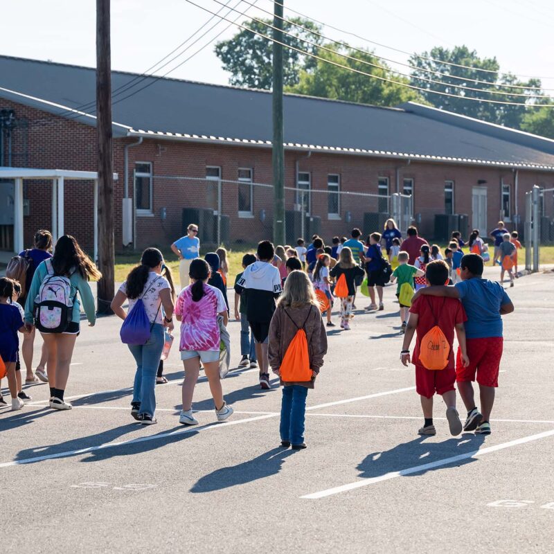 A large group of children pictured from behind as they walk into a school building.