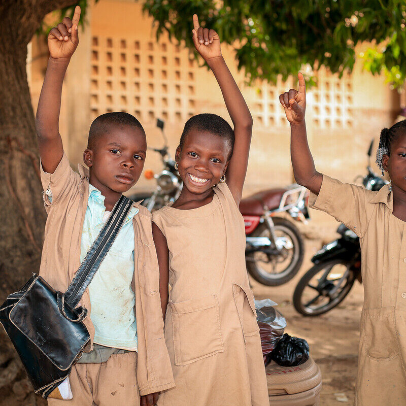 children smiling pointing hands up with pointer finger extended.